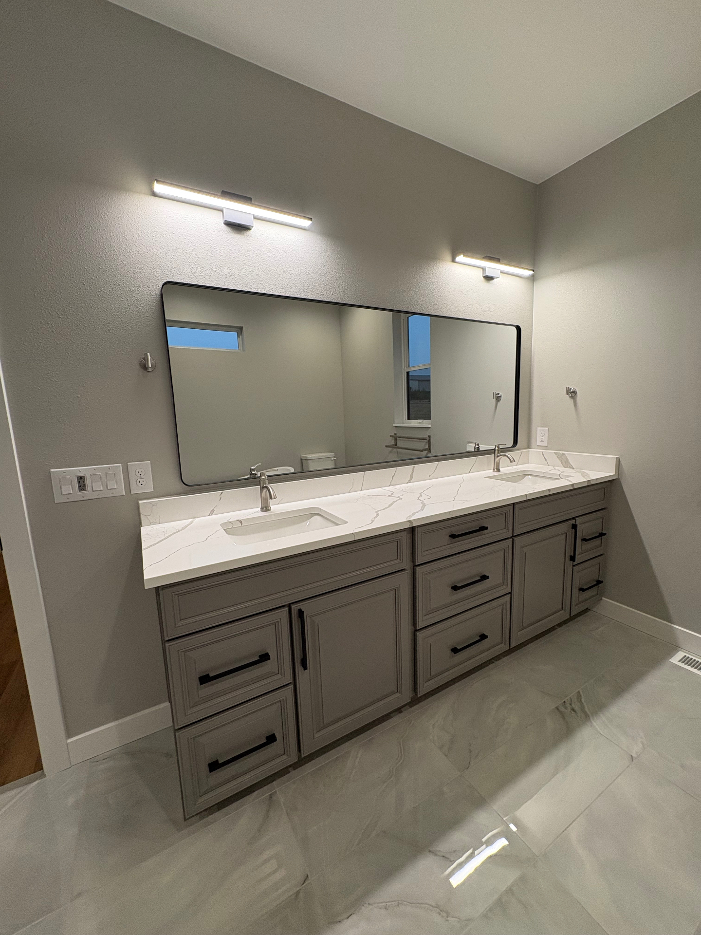 Custom grey double vanity with quartz top, black hardware and wide framed mirror