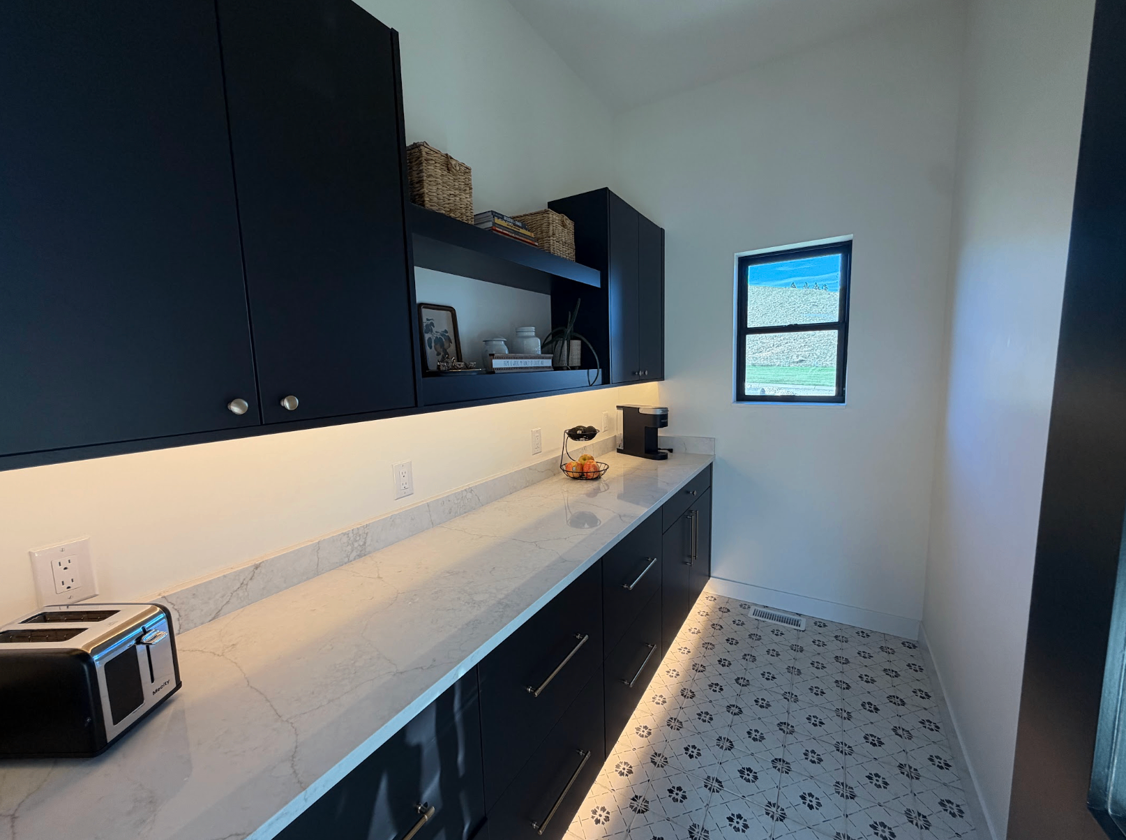 Kitchen counter with dark navy cabinetry, marble counter, under cabinet lighting and patterned tile floor