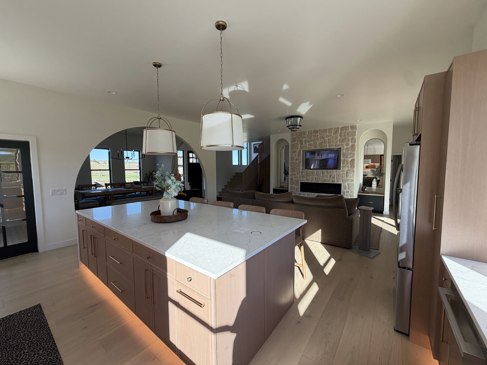 Kitchen island with a white marble counter and brass pendants, arched opening to the dining room and a stone fireplace beyond
