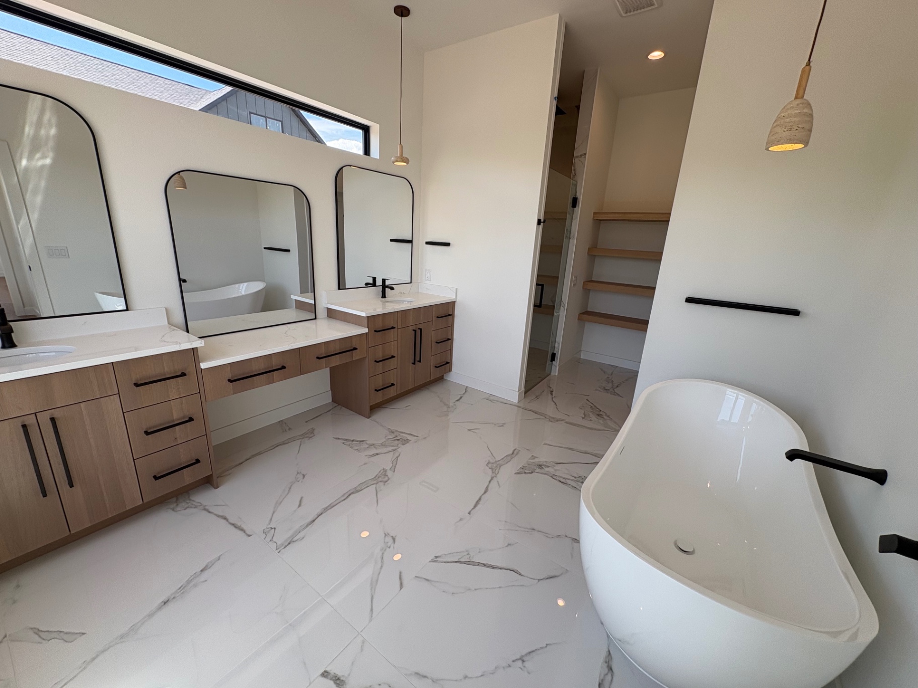 Primary bath with double oak vanities, arched black mirrors, marble-look porcelain floor and freestanding tub