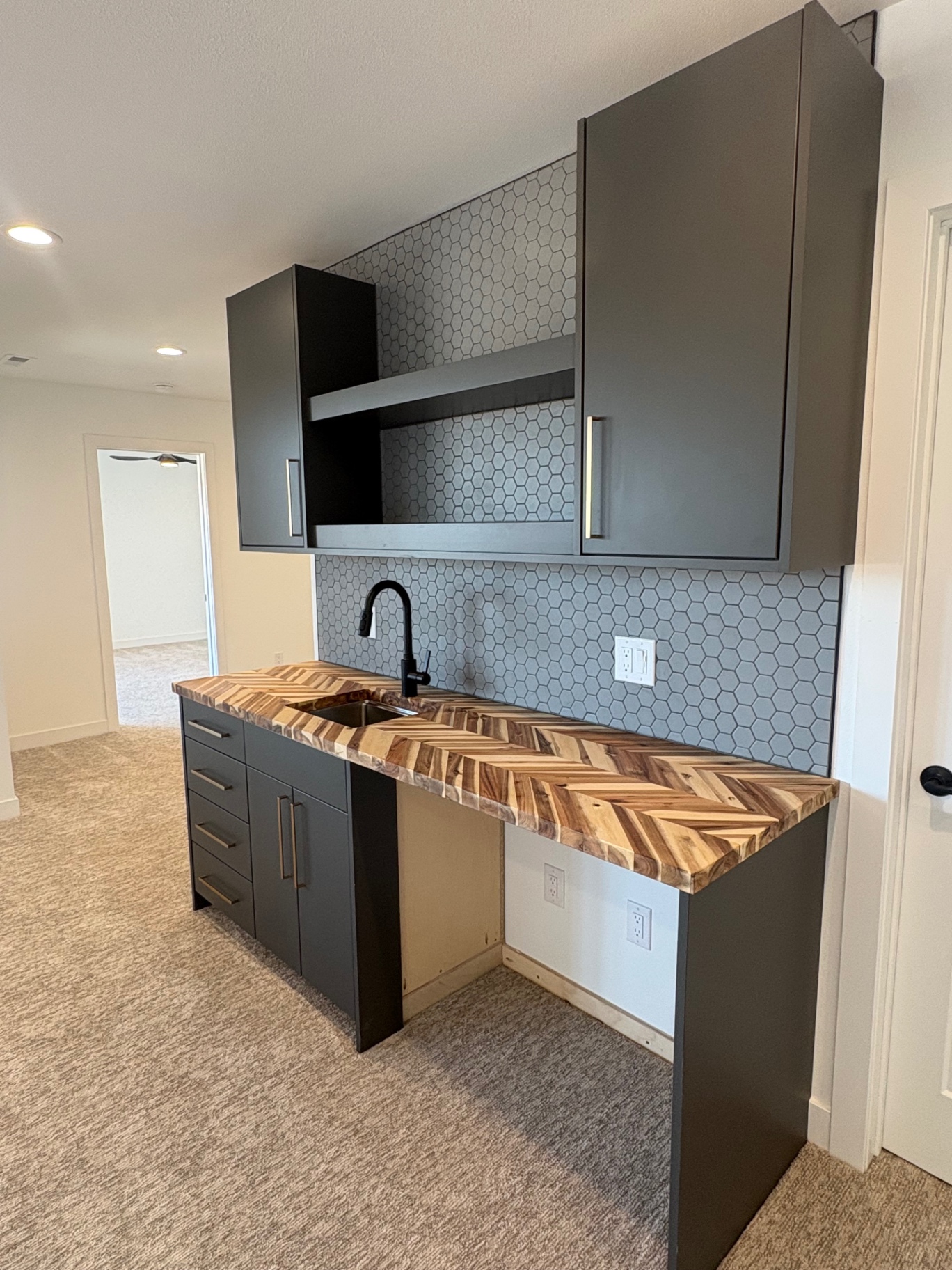 Basement wet bar with charcoal cabinetry, chevron butcher block top and hexagon tile backsplash