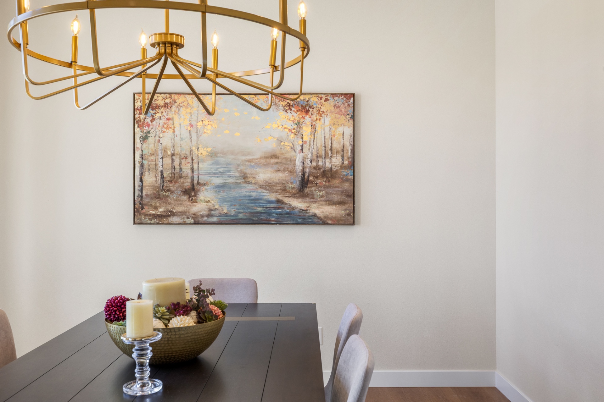 Dining room with brass ring chandelier, dark table and framed landscape art