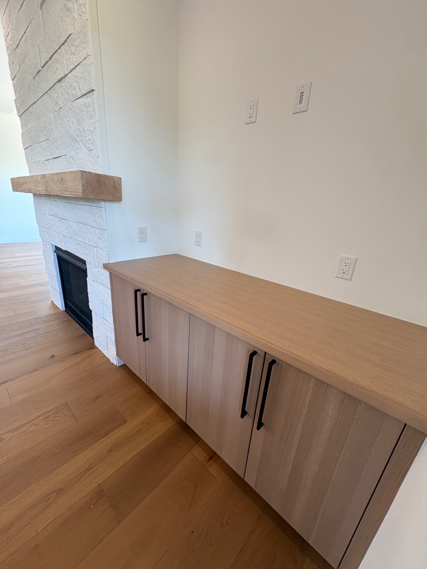 Custom white oak credenza built-in beside a stone fireplace on wide-plank floors