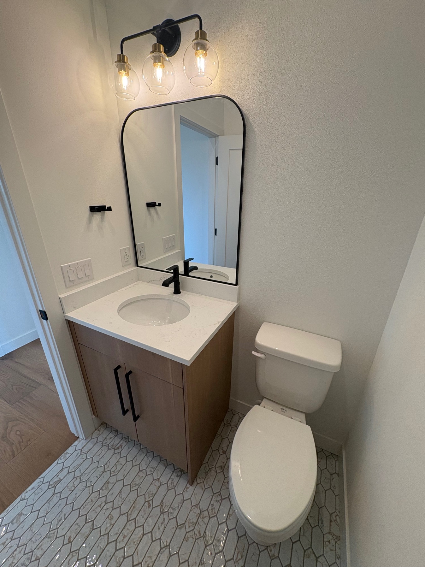 Powder bath with stained oak vanity, quartz top, arched black mirror and marble hex tile floor