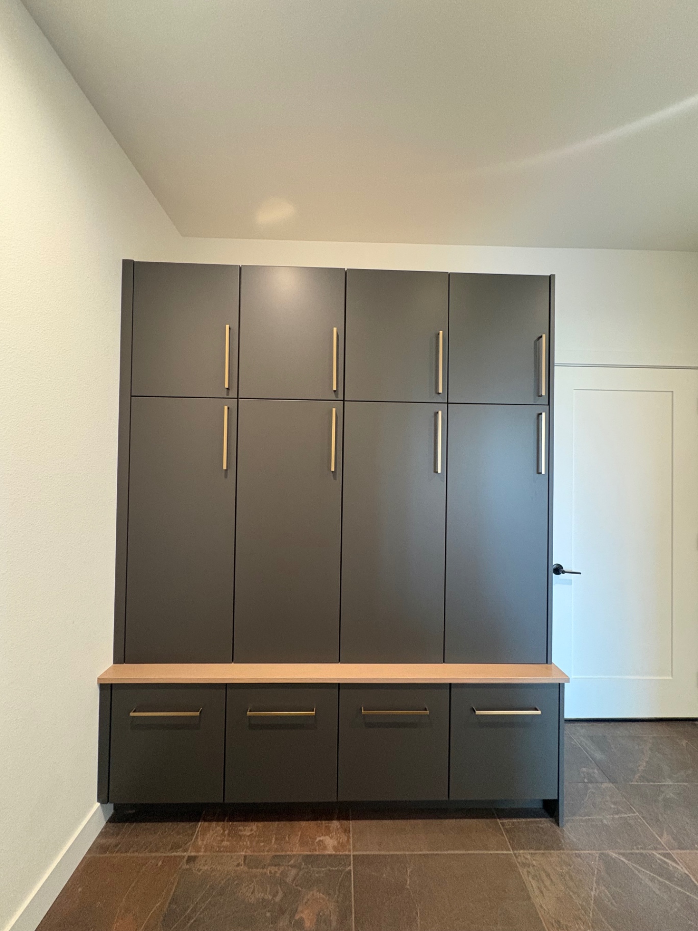 Full-height charcoal mudroom lockers with brass pulls and white oak bench top