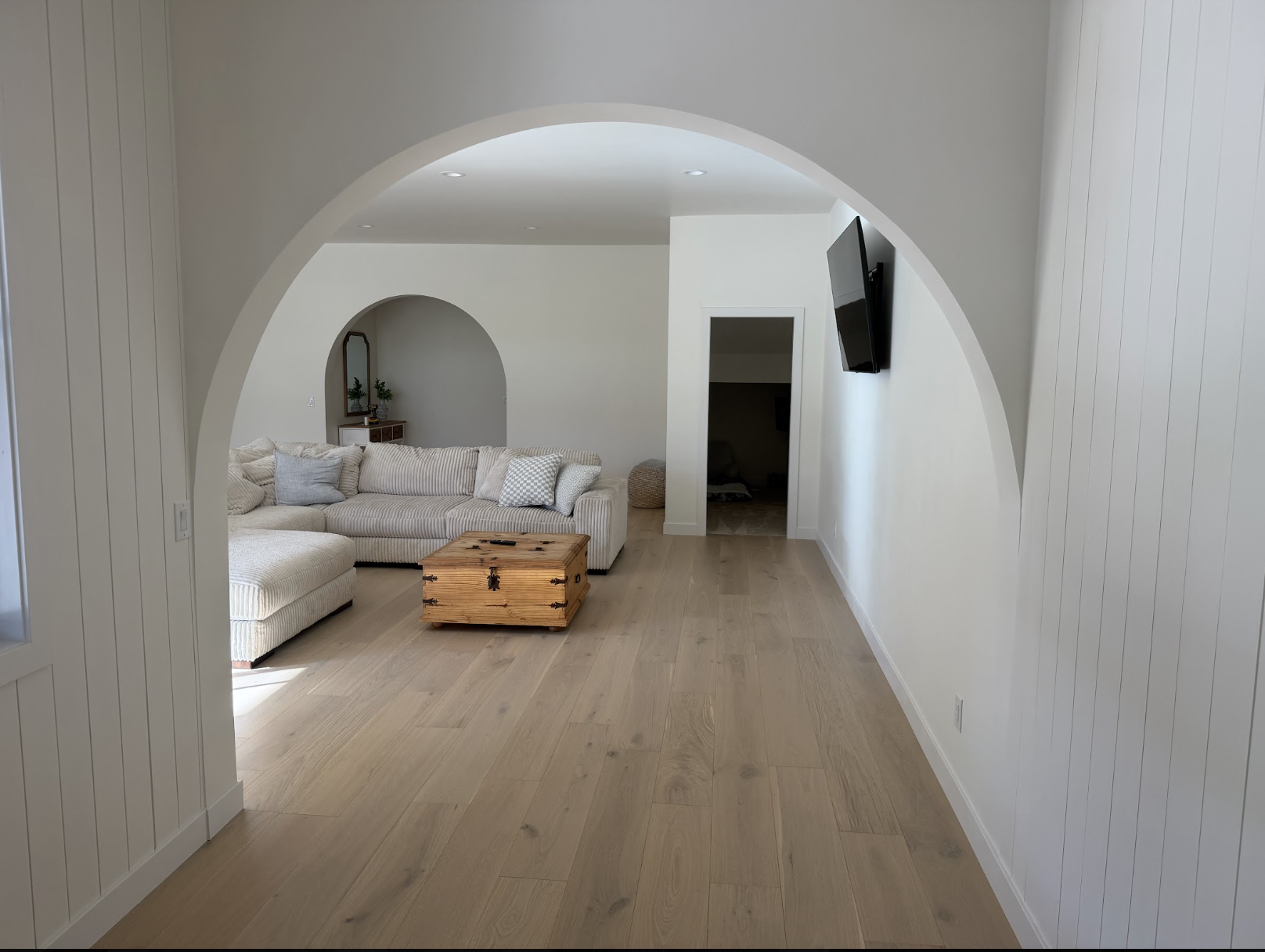 Arched opening into the living room with white oak floors, striped sectional sofa and wood coffee chest