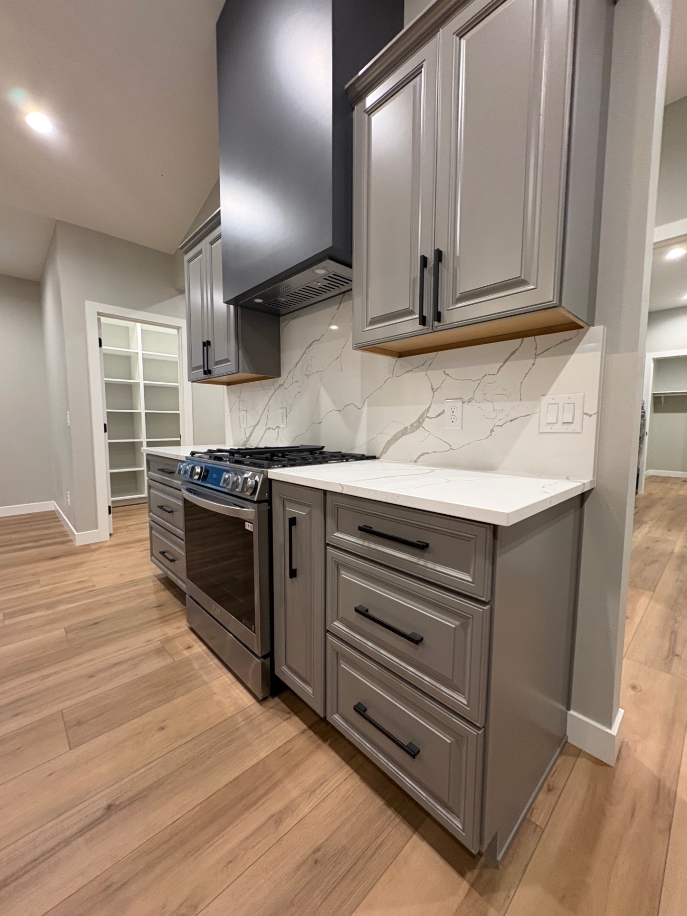 Kitchen range wall with grey painted cabinetry, quartz slab backsplash and custom hood