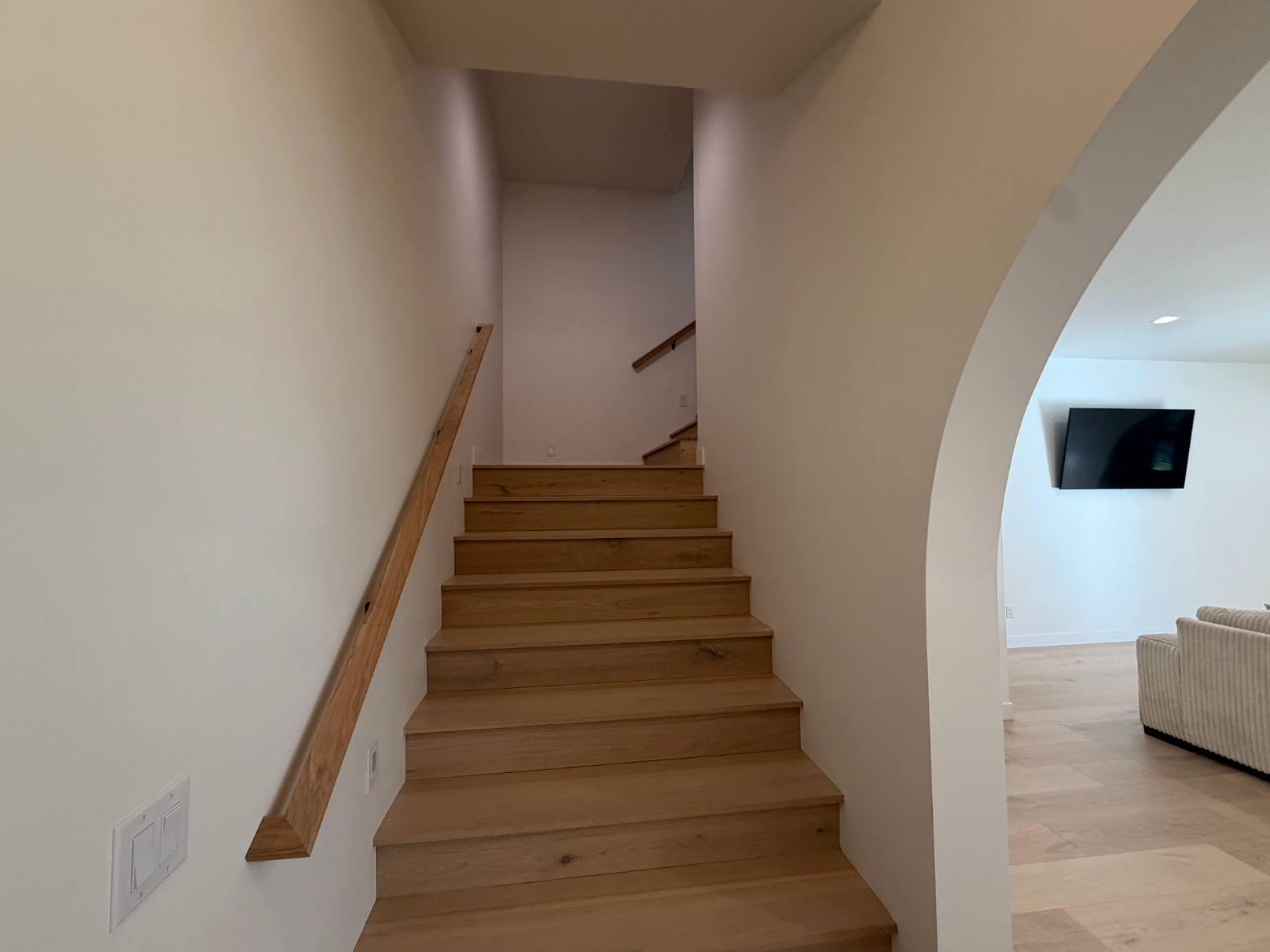 White oak lower stair beside a wide arched opening into the family room