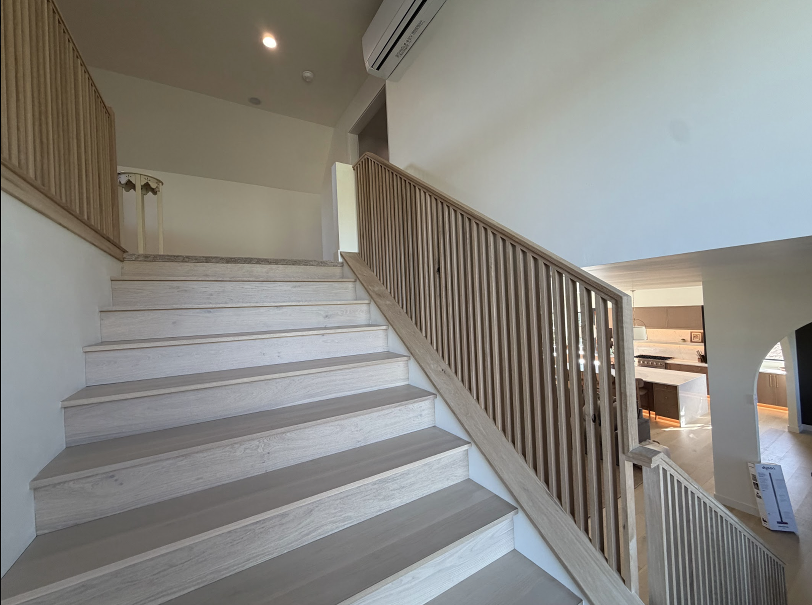 White oak stair with a floor to ceiling slat railing and view into the kitchen