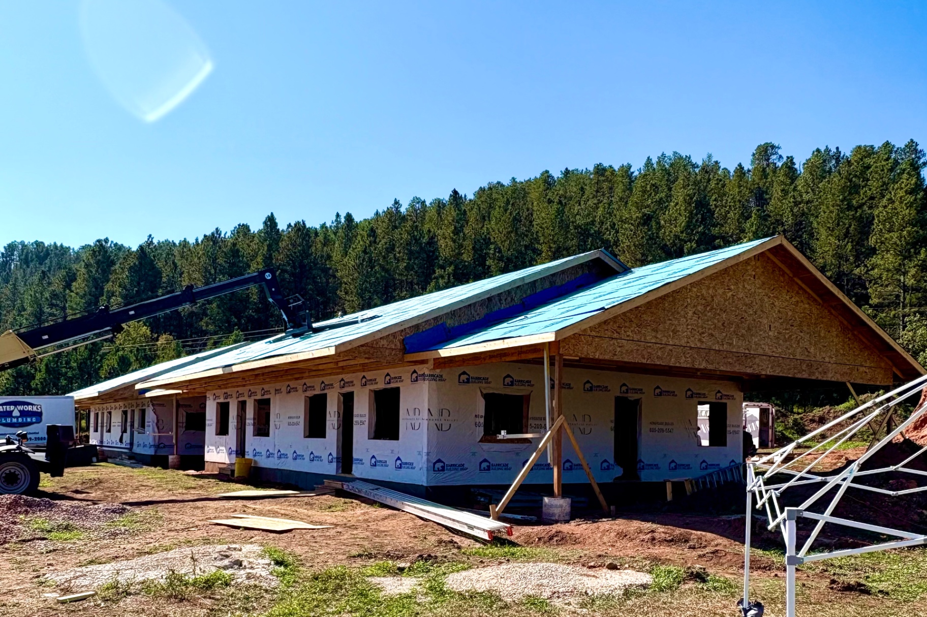 Custom home framing with gable trusses and roof sheathing under a clear Black Hills sky