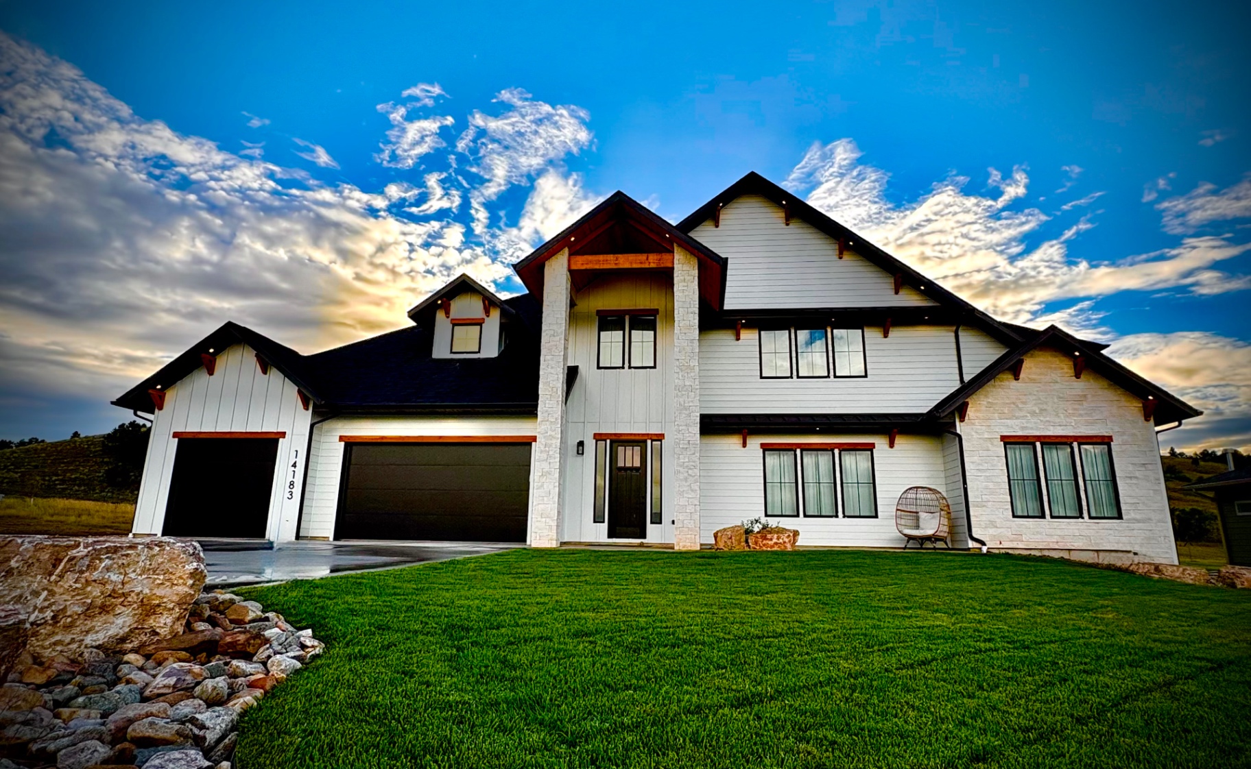 Two-story custom home at dusk with white stone, board-and-batten siding and stained timber accents