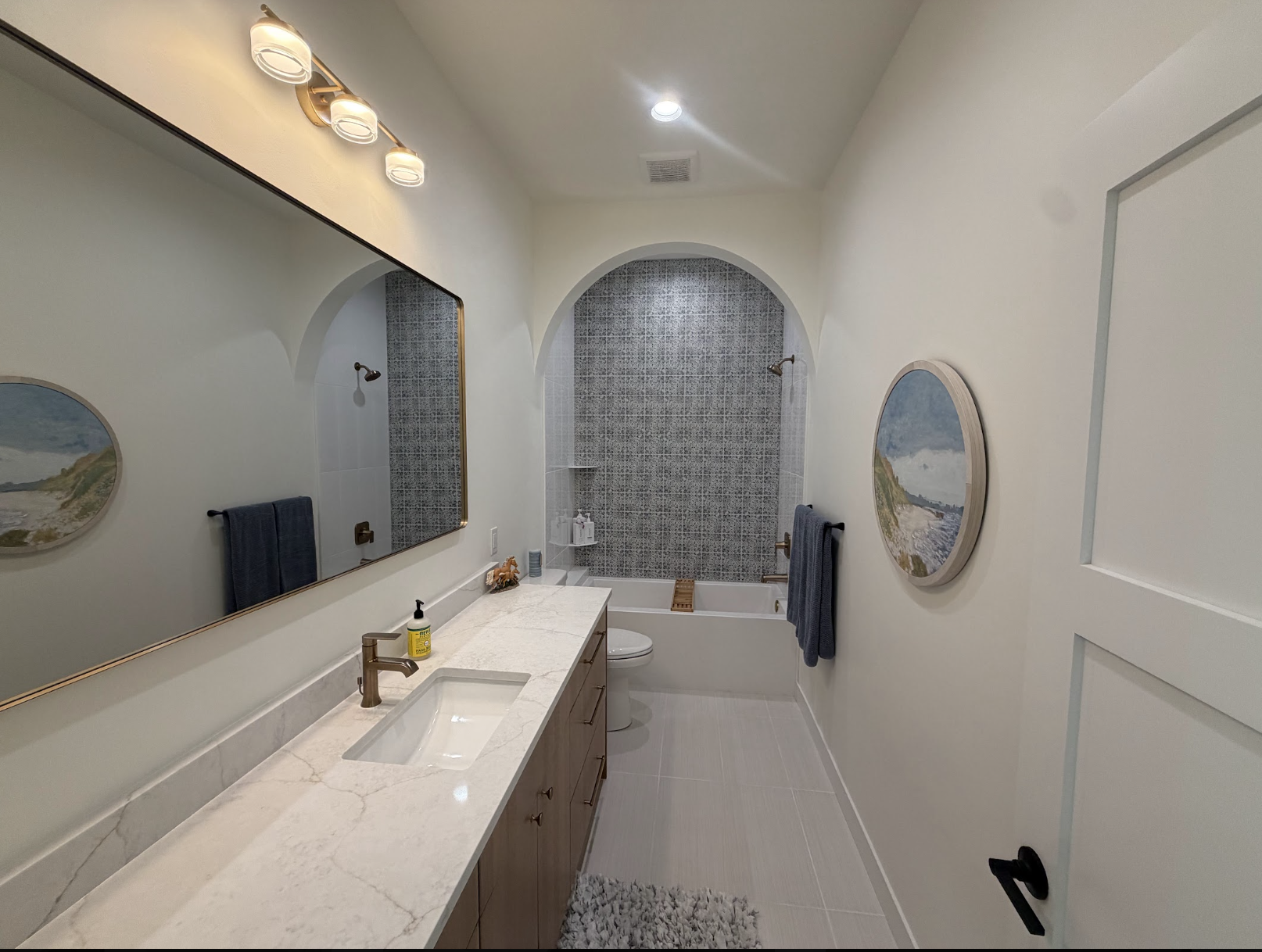 Bathroom with a freestanding tub inside an arched alcove of blue and white patterned tile, gold sconces and double vanity