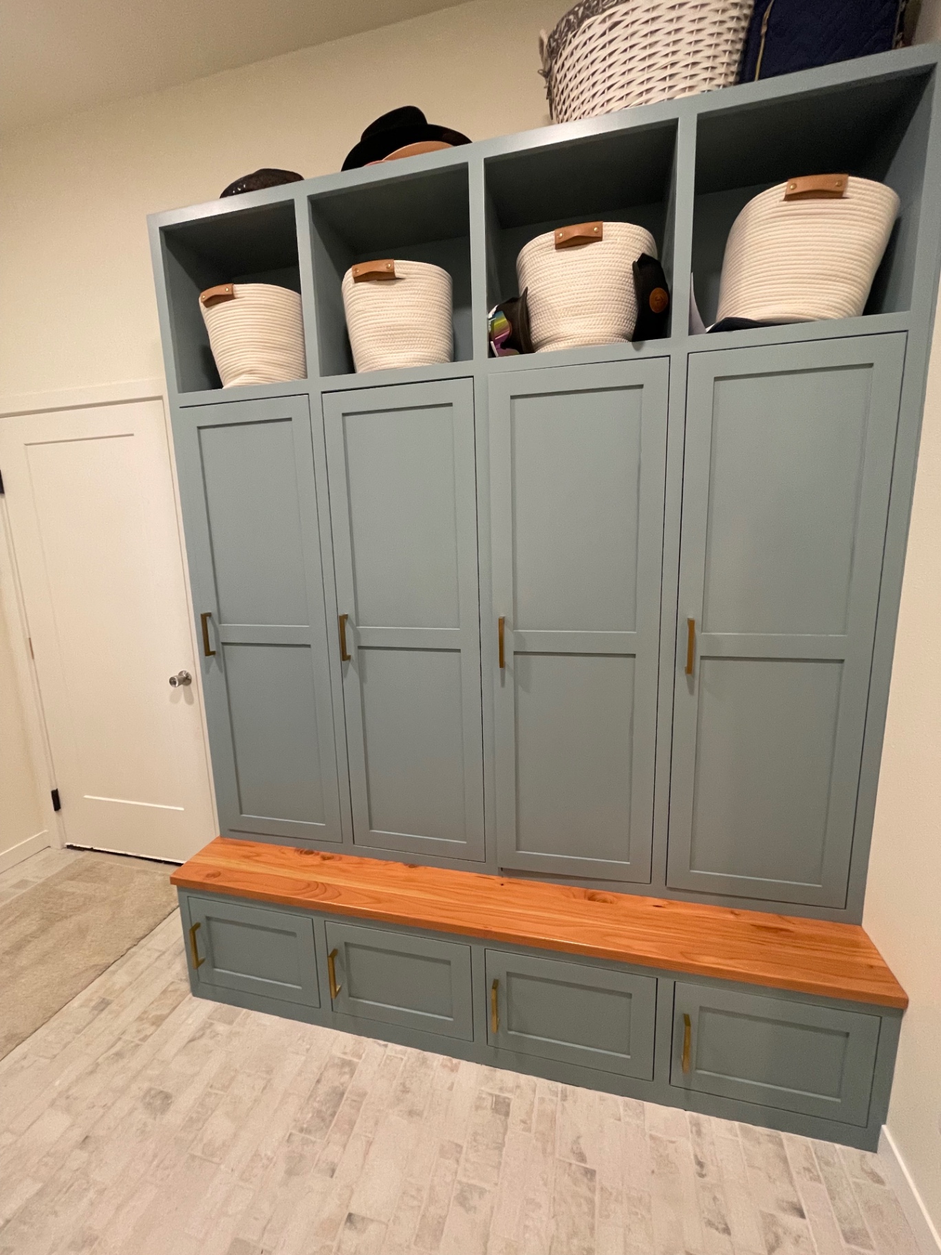 Custom mudroom lockers in soft teal with a solid wood bench top and brass pulls