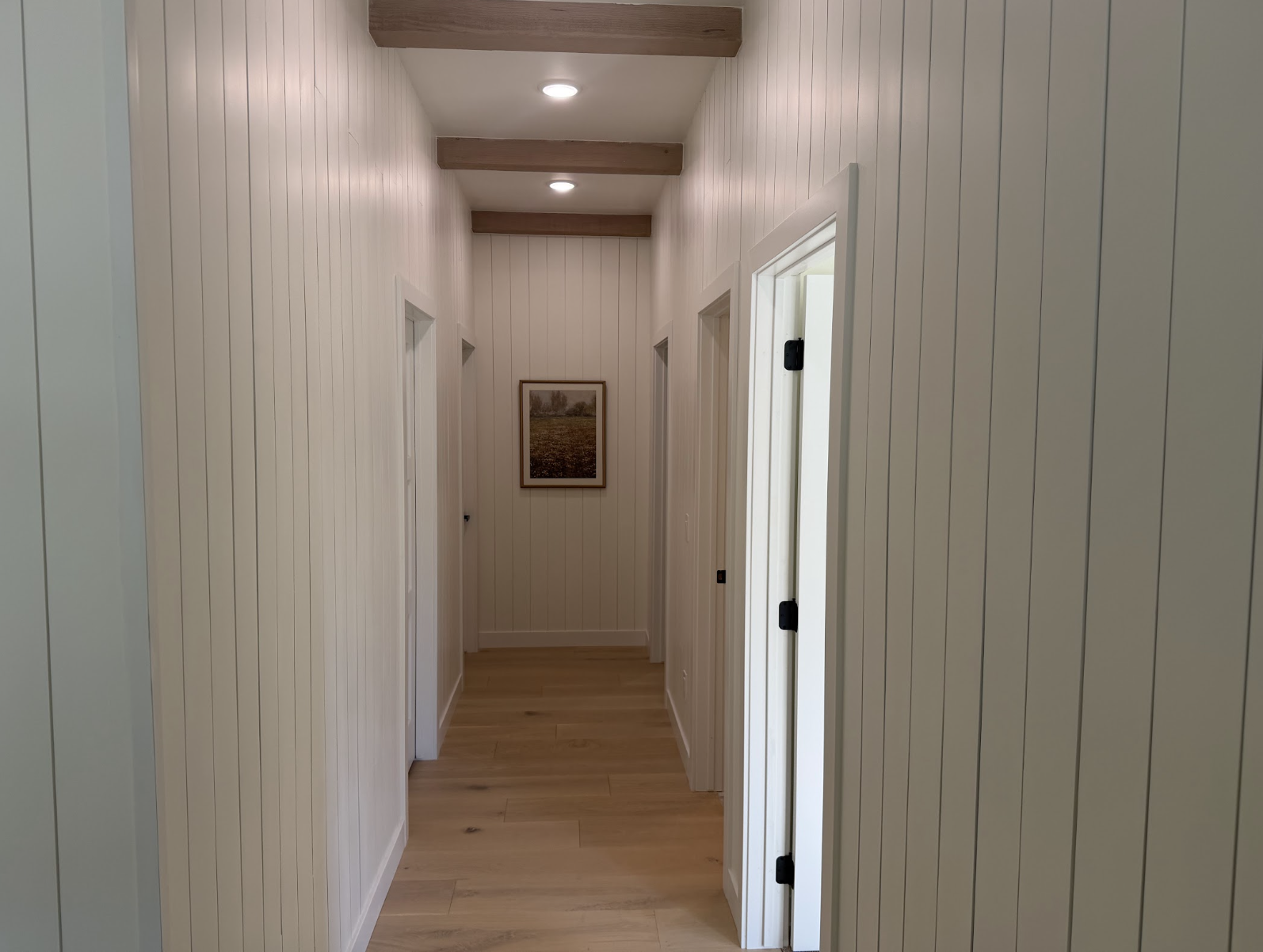 Hallway with vertical white panel walls, natural wood ceiling beams and white oak floors