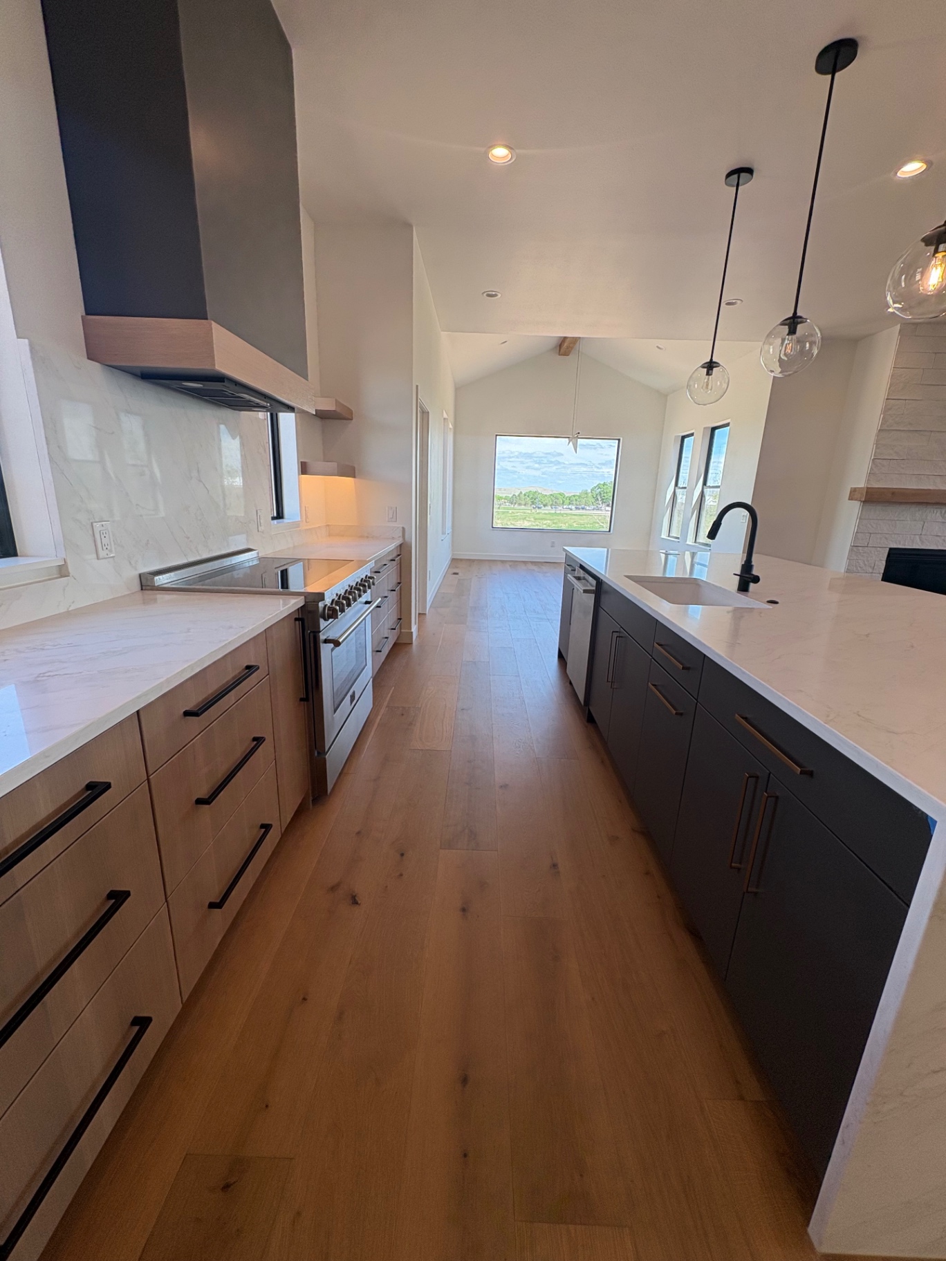 Galley kitchen with white oak drawer bases, marble-look quartz, professional range and long charcoal island