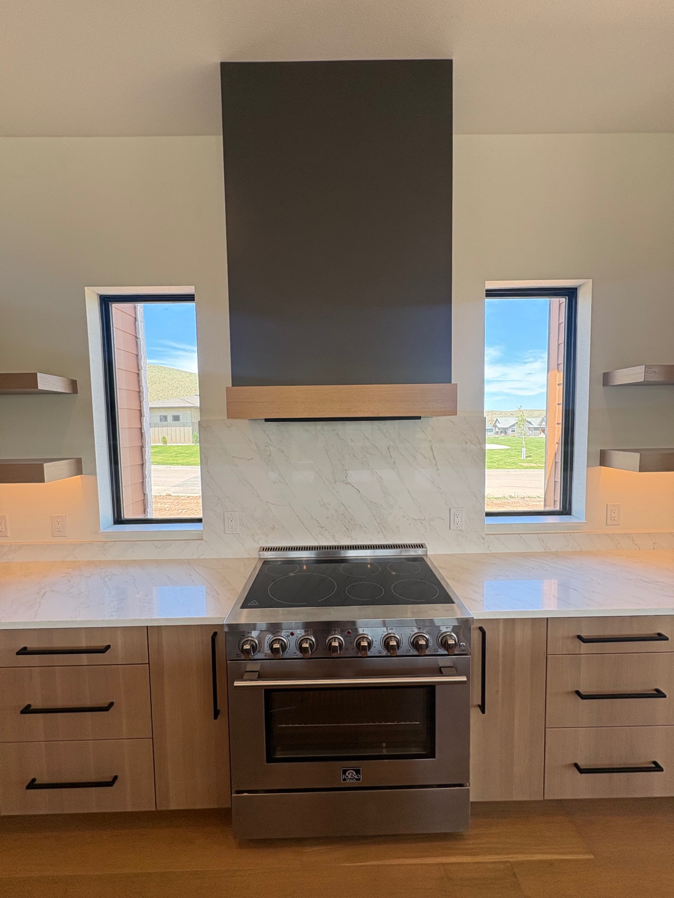 Custom hood shroud with white oak band flanked by windows and full-height quartz backsplash
