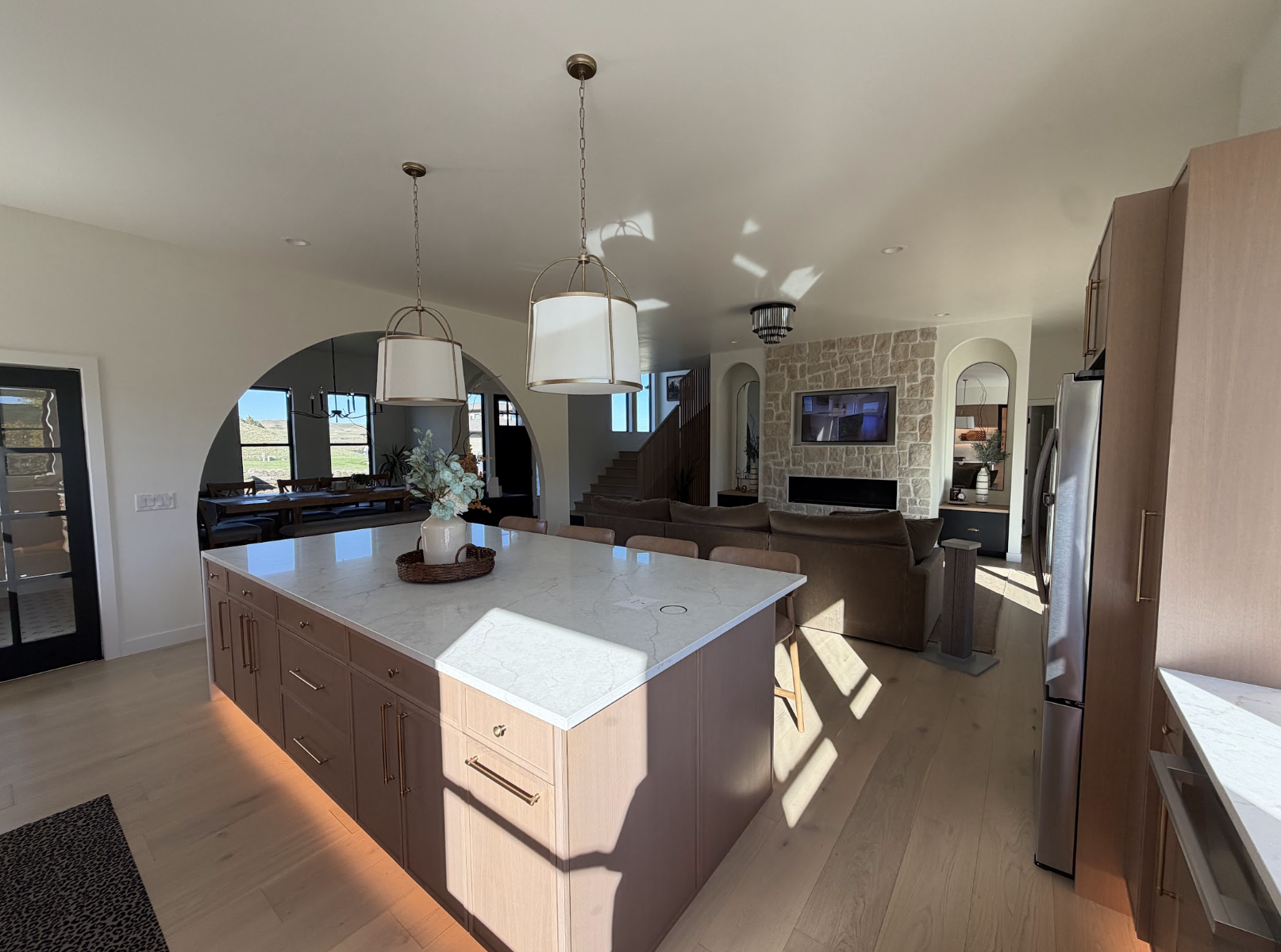Wide kitchen view with a large quartz island, warm wood cabinetry and open great room beyond