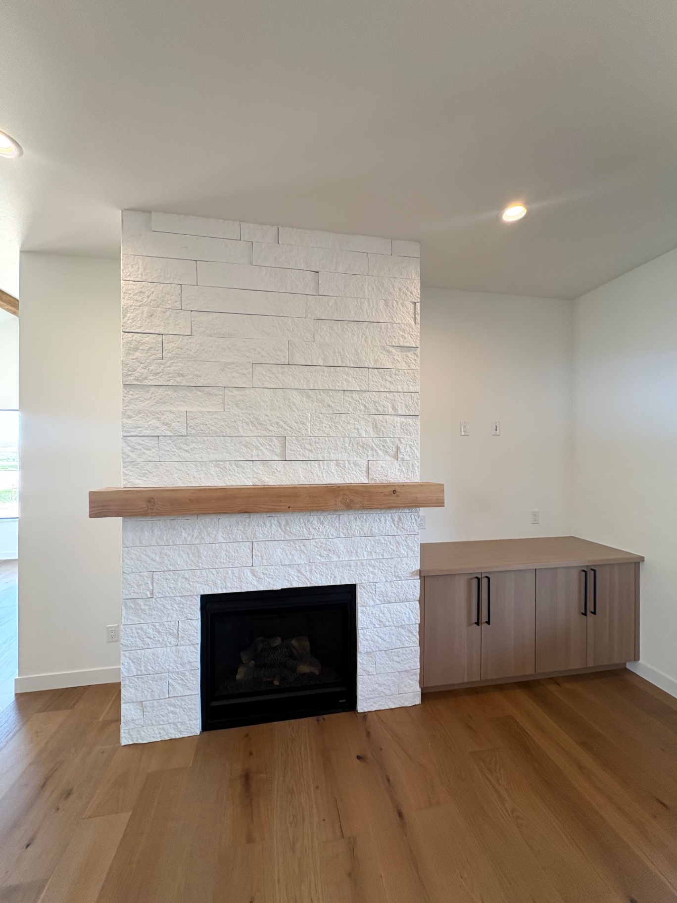 White stacked stone fireplace with timber mantel and custom oak credenza