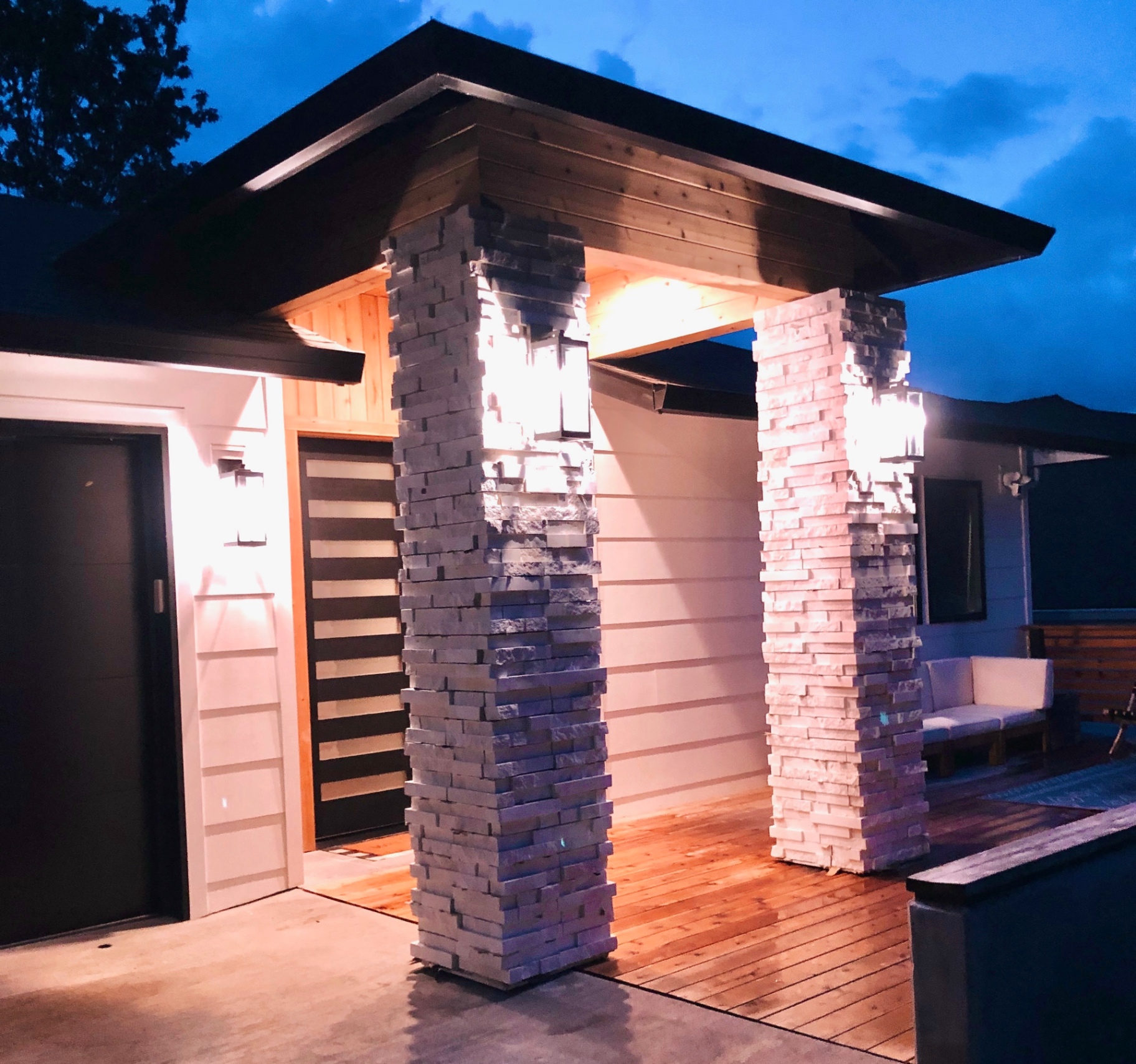 Covered entry at dusk with stacked stone columns, cedar ceiling and warm uplighting