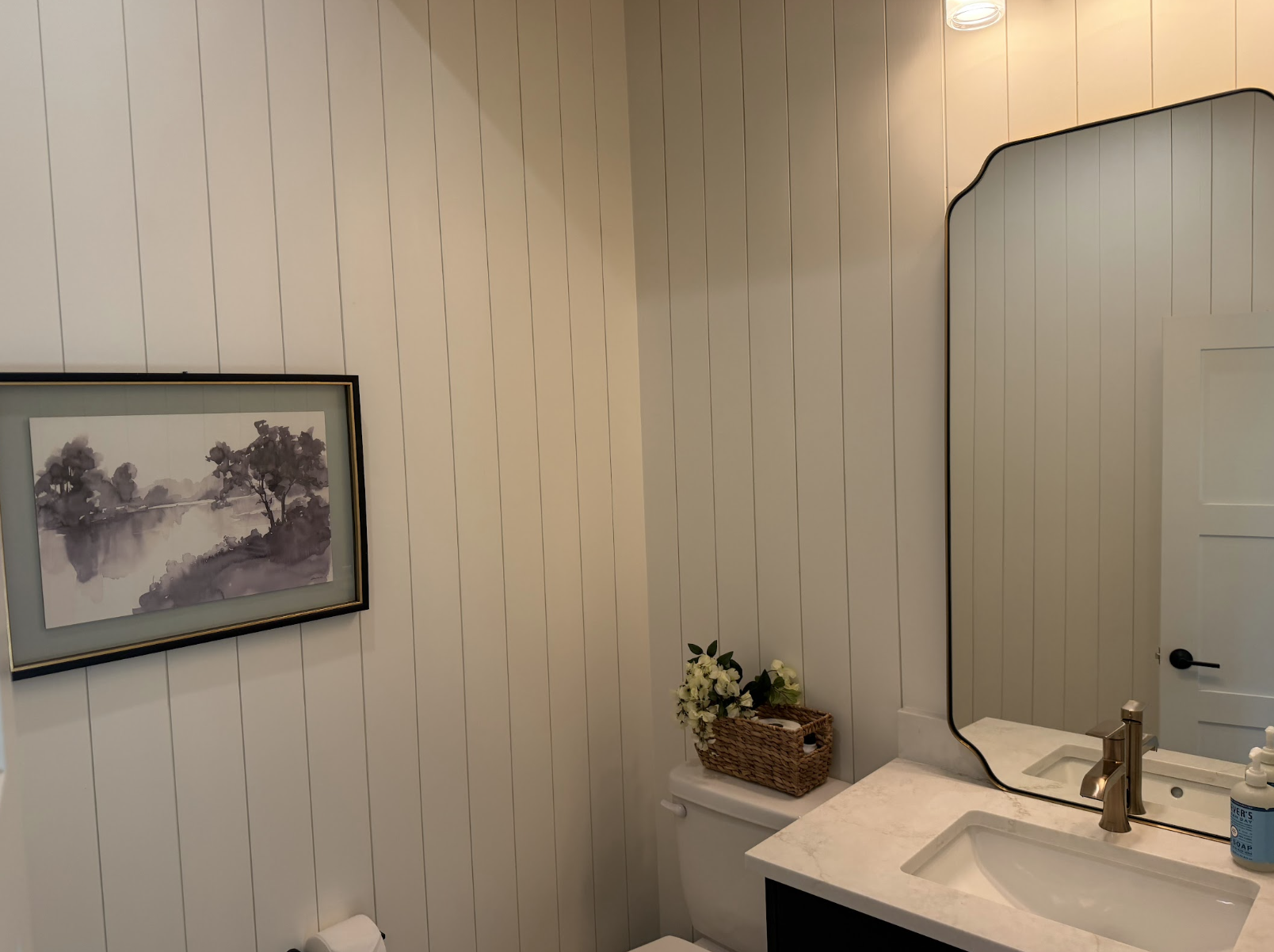 Powder bathroom with vertical paneled walls, a dark vanity, quartz counter and shaped black mirror
