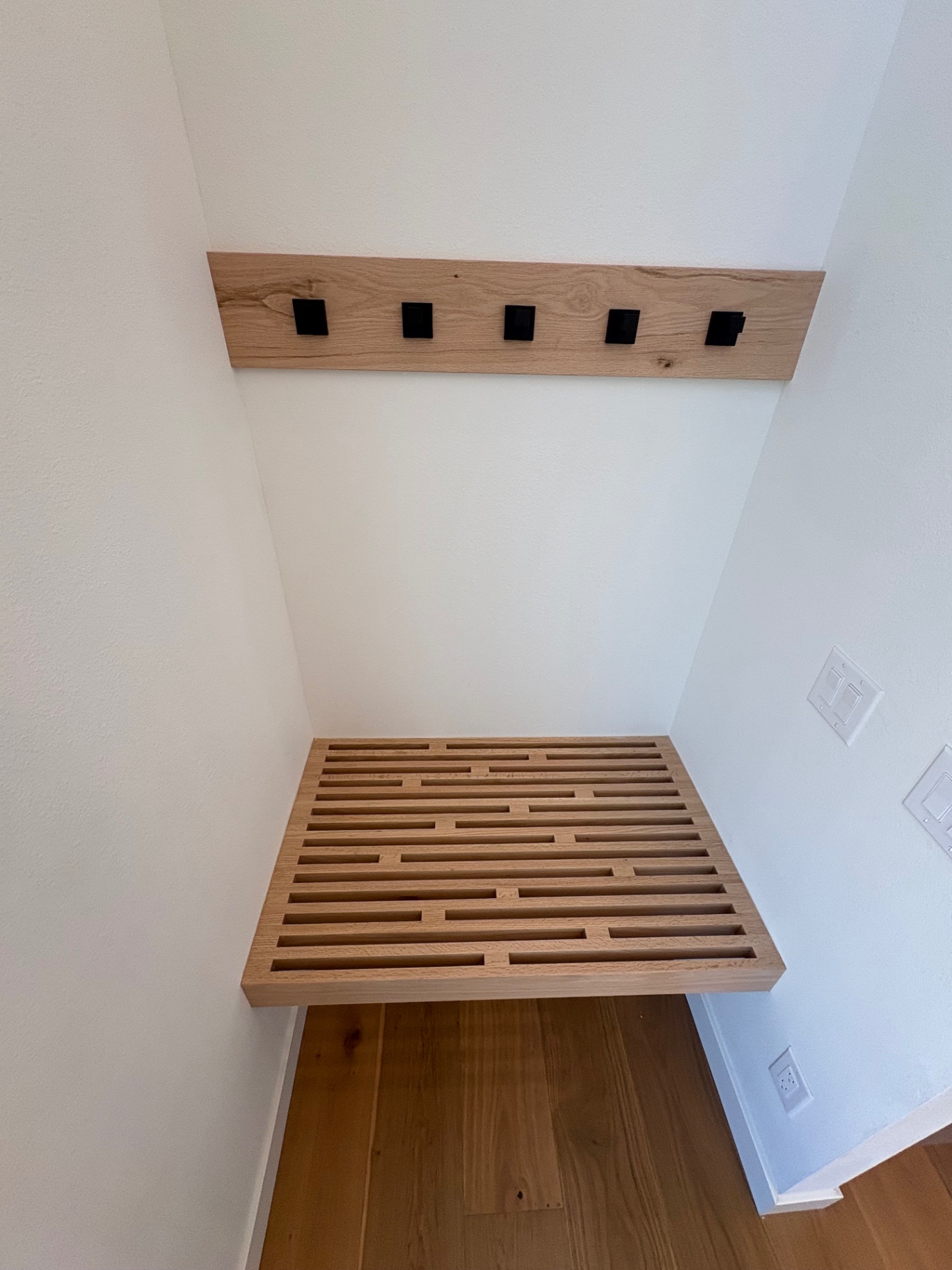 Custom floating white oak slat bench with matching hook rail in a drop zone