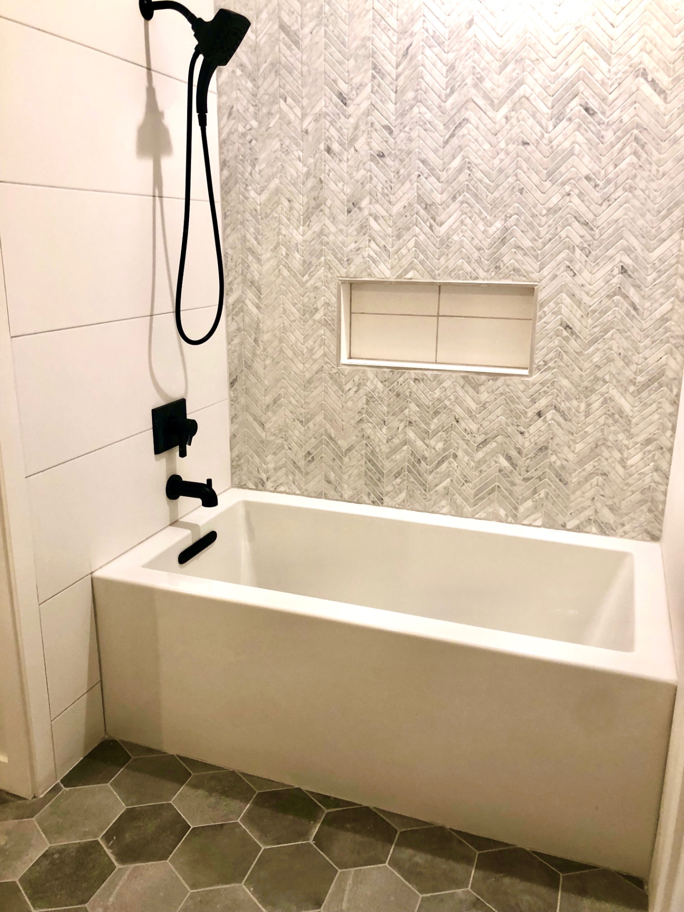 Guest bath with marble herringbone tile surround and matte black fixtures