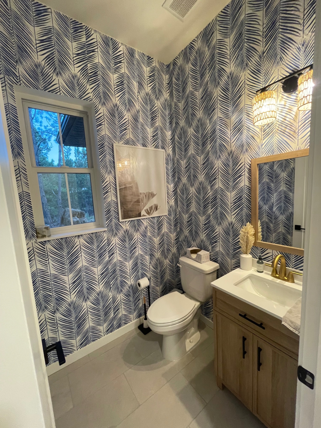 Powder bath with patterned wallpaper, oak vanity, brass fixtures and woven sconces