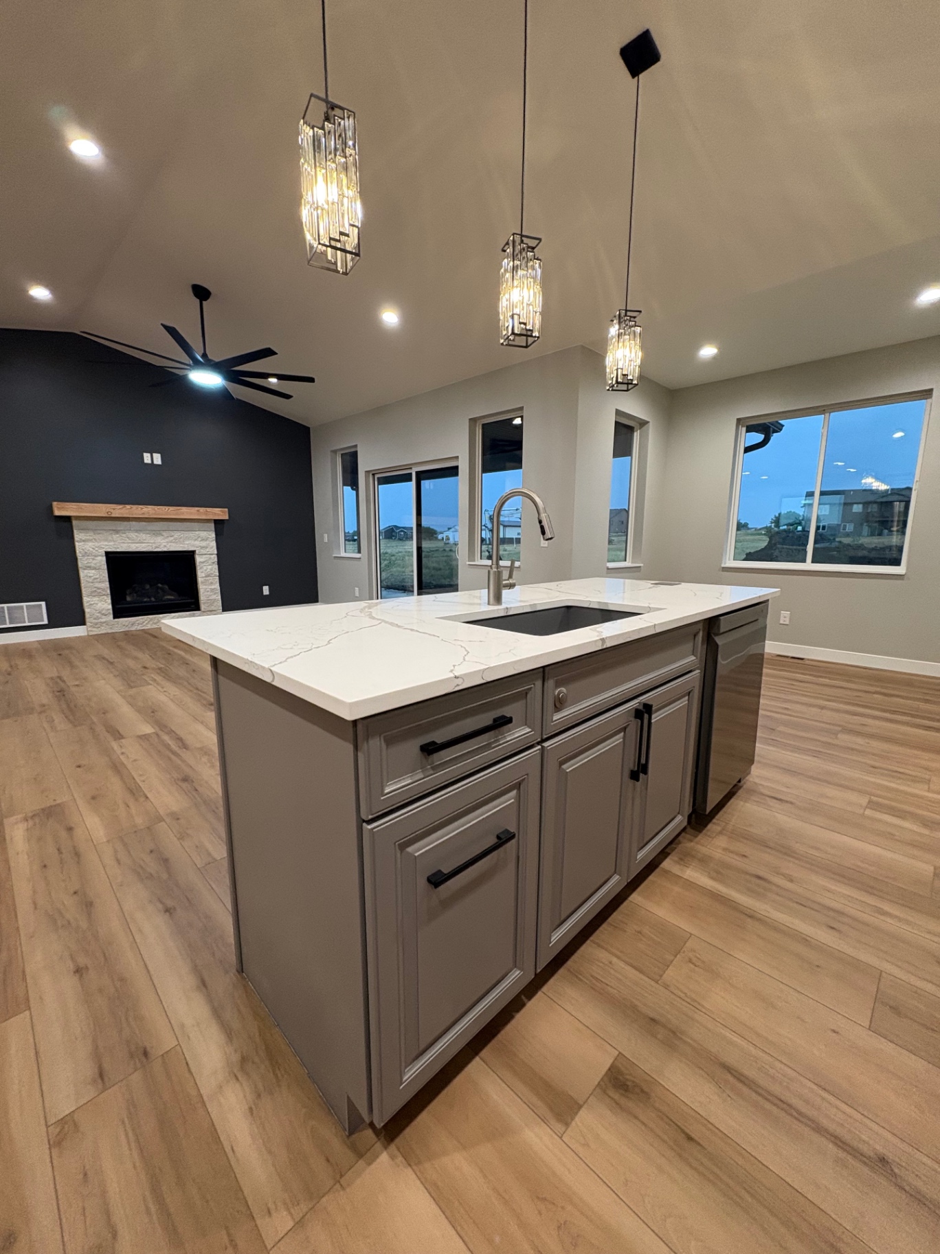 Open kitchen island with quartz top overlooking a stone fireplace and vaulted great room at dusk