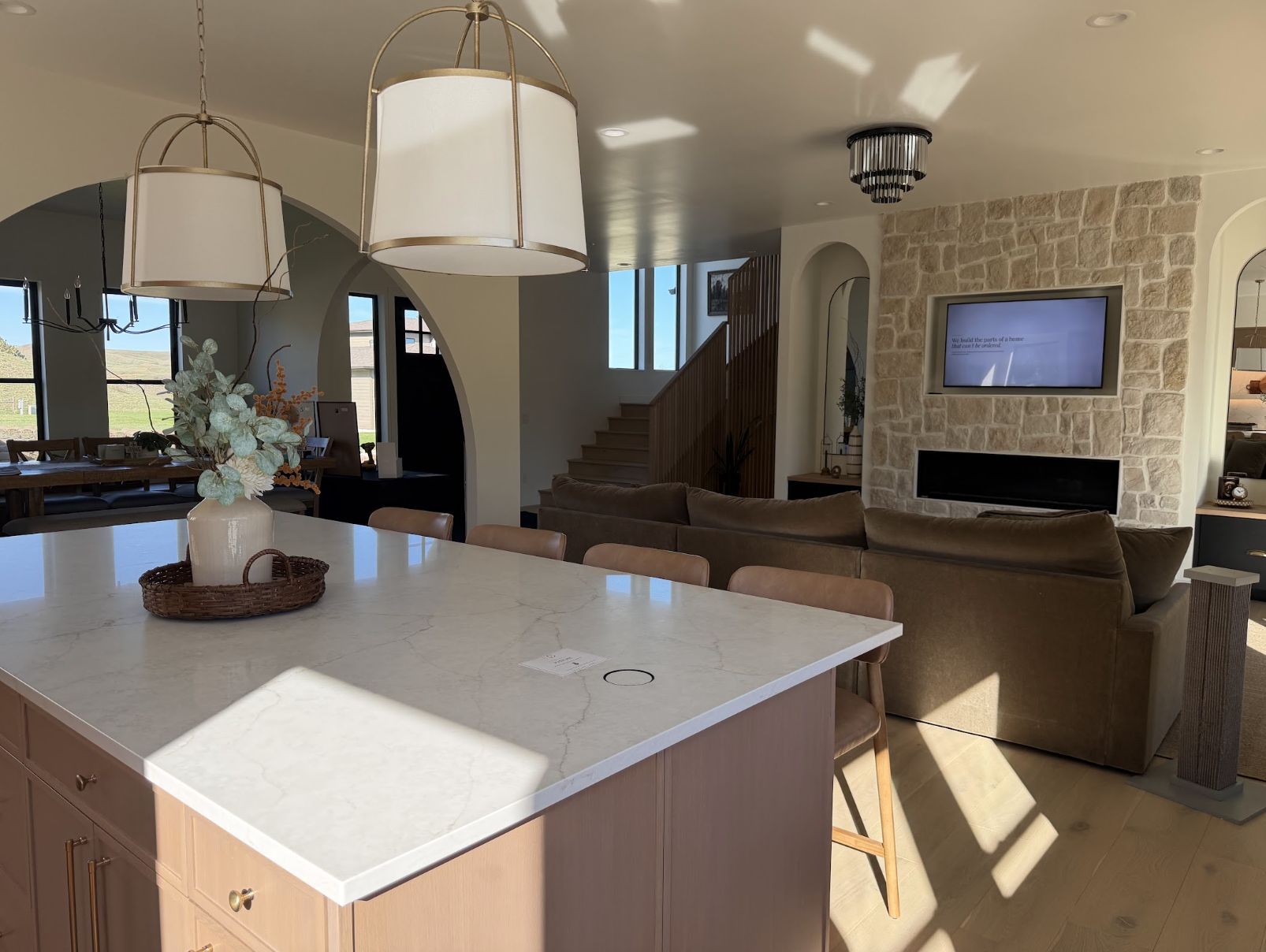 Oversized kitchen island with a white marble counter, brass lantern pendants and a stone fireplace with a mounted TV behind