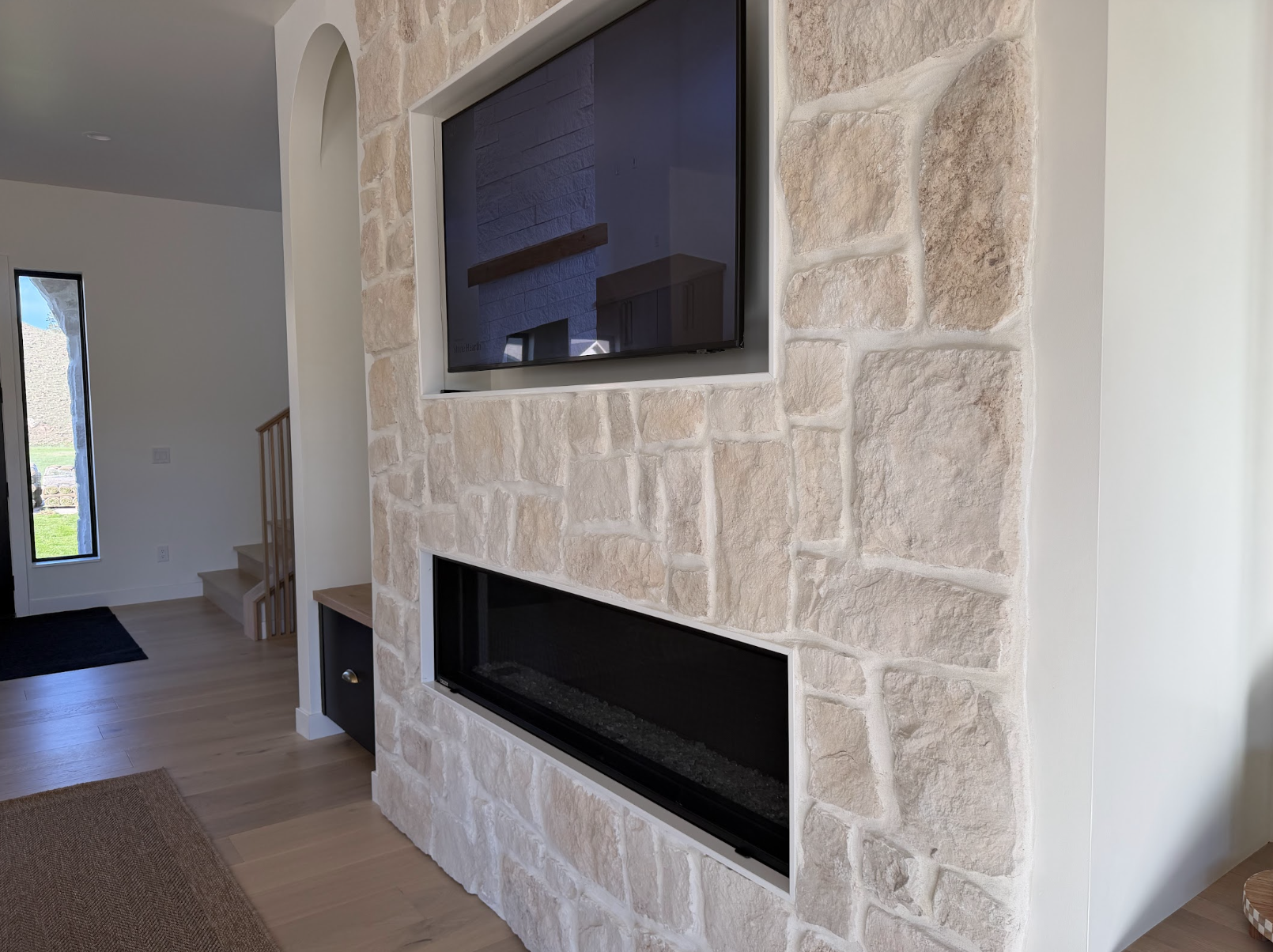 Great room fireplace faced in light stone with a long black firebox and recessed television