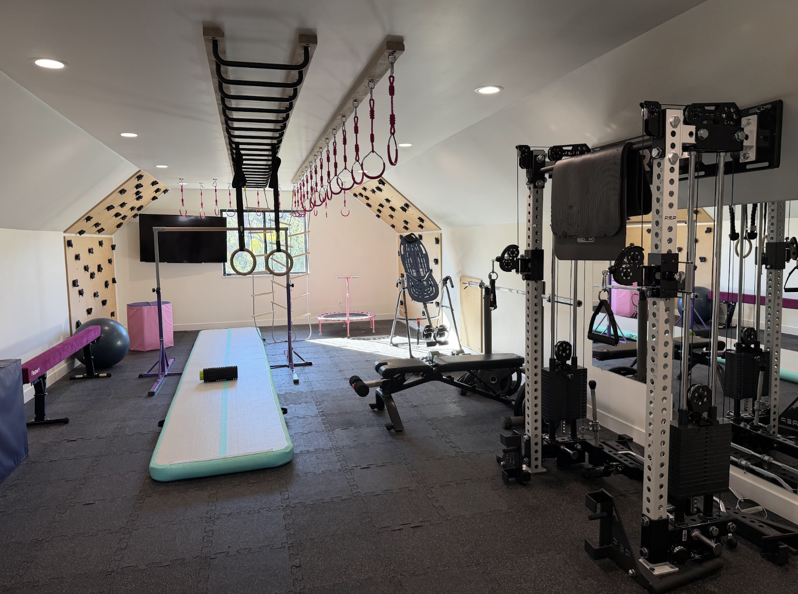 Bonus room gym with climbing wall panels, hanging rings, monkey bars, gymnastics mats and a weight rack