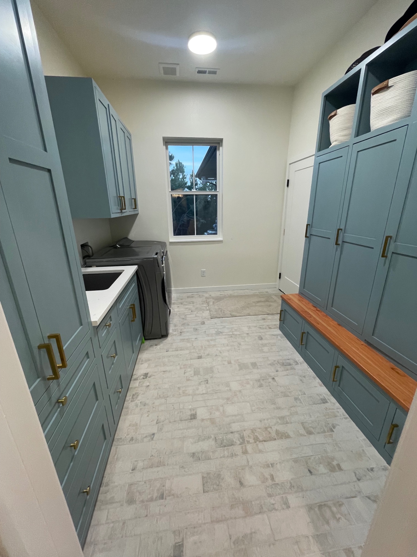 Combined laundry and mudroom with teal cabinetry, brick-look tile floor and wood bench