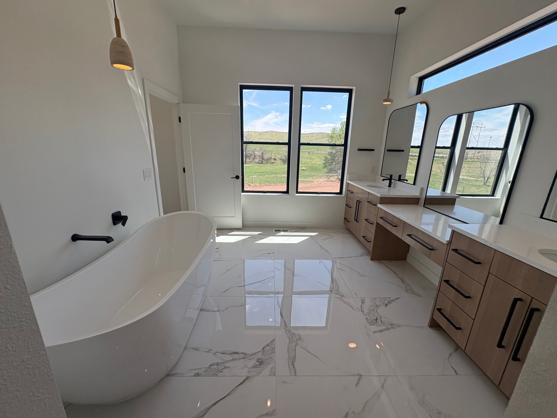 Freestanding soaking tub with matte black wall filler and prairie views through black-framed windows