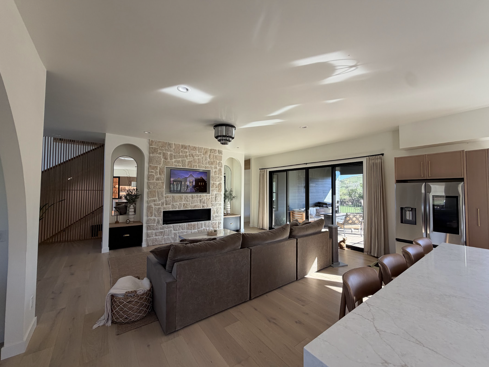 Great room with a white stone fireplace, mounted TV, brown sectional sofa, arched niches and doors to the covered deck