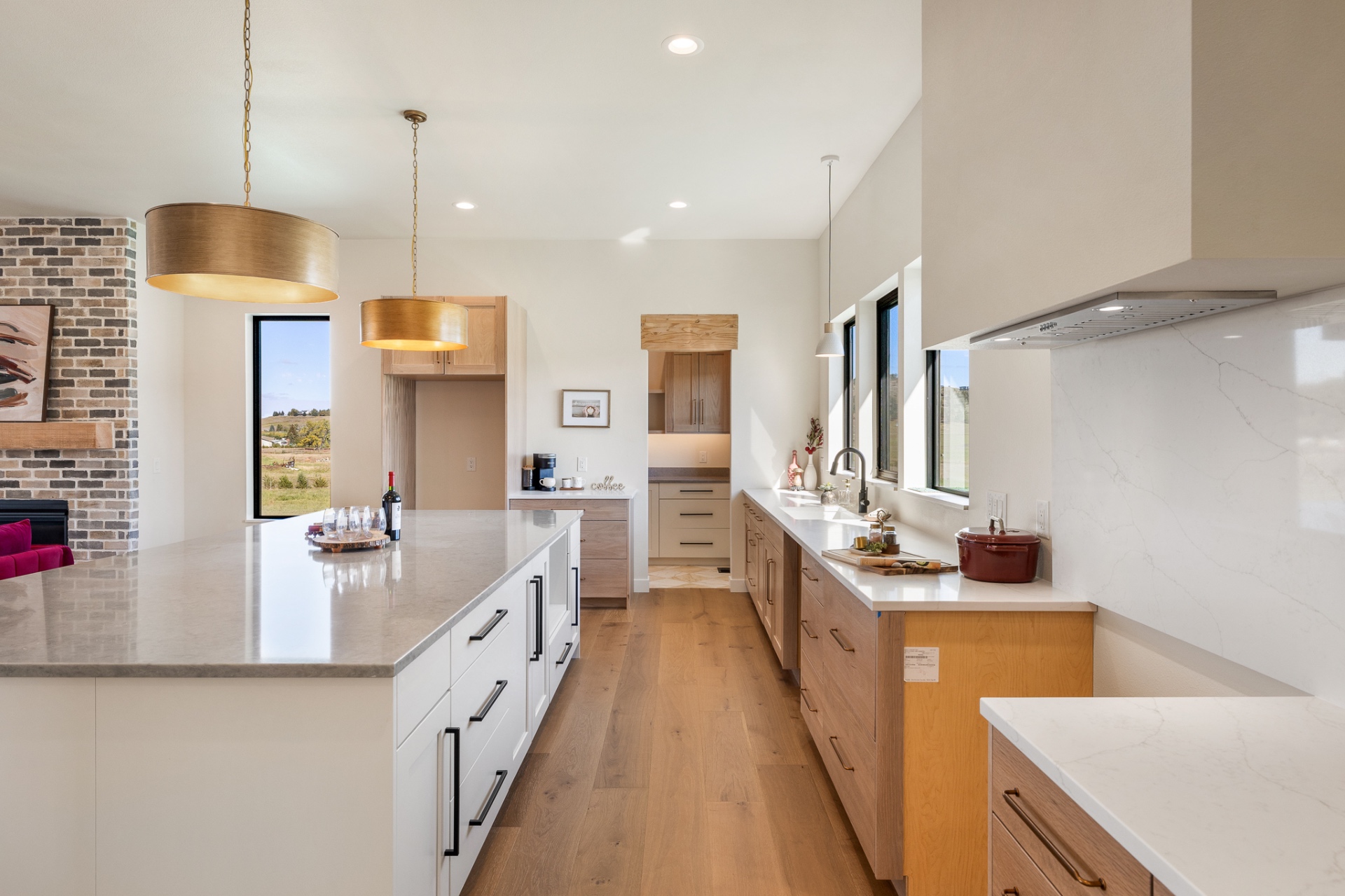 Custom kitchen with white oak cabinetry, quartz island, brass drum pendants and brick fireplace beyond