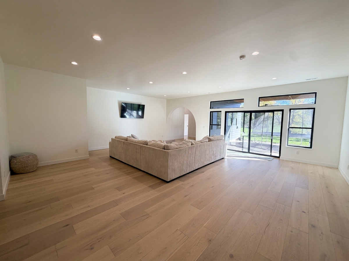 Open family room with white oak flooring, black framed windows and doors to the backyard